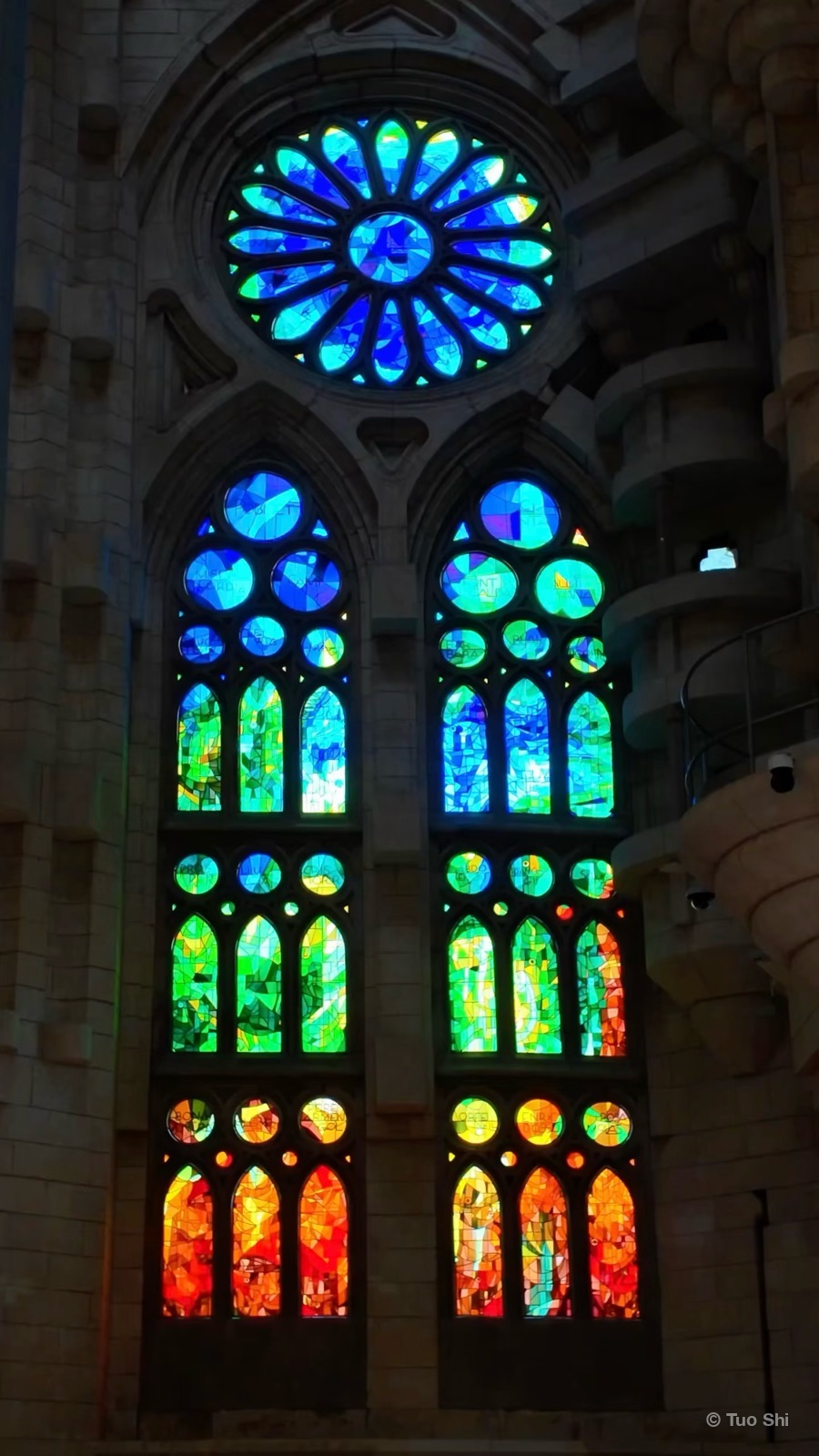 A rose window and tall stained-glass windows glowing blue, green, and orange