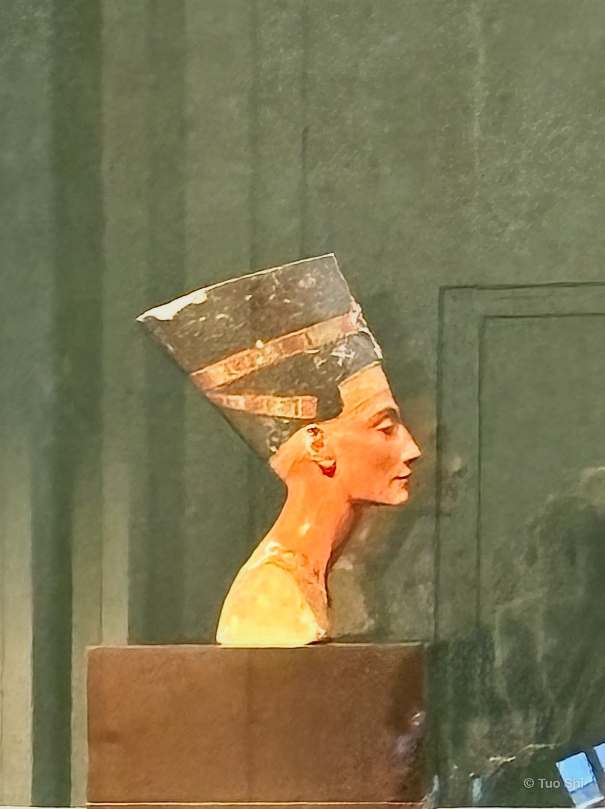 The painted bust of Nefertiti in profile against a green wall