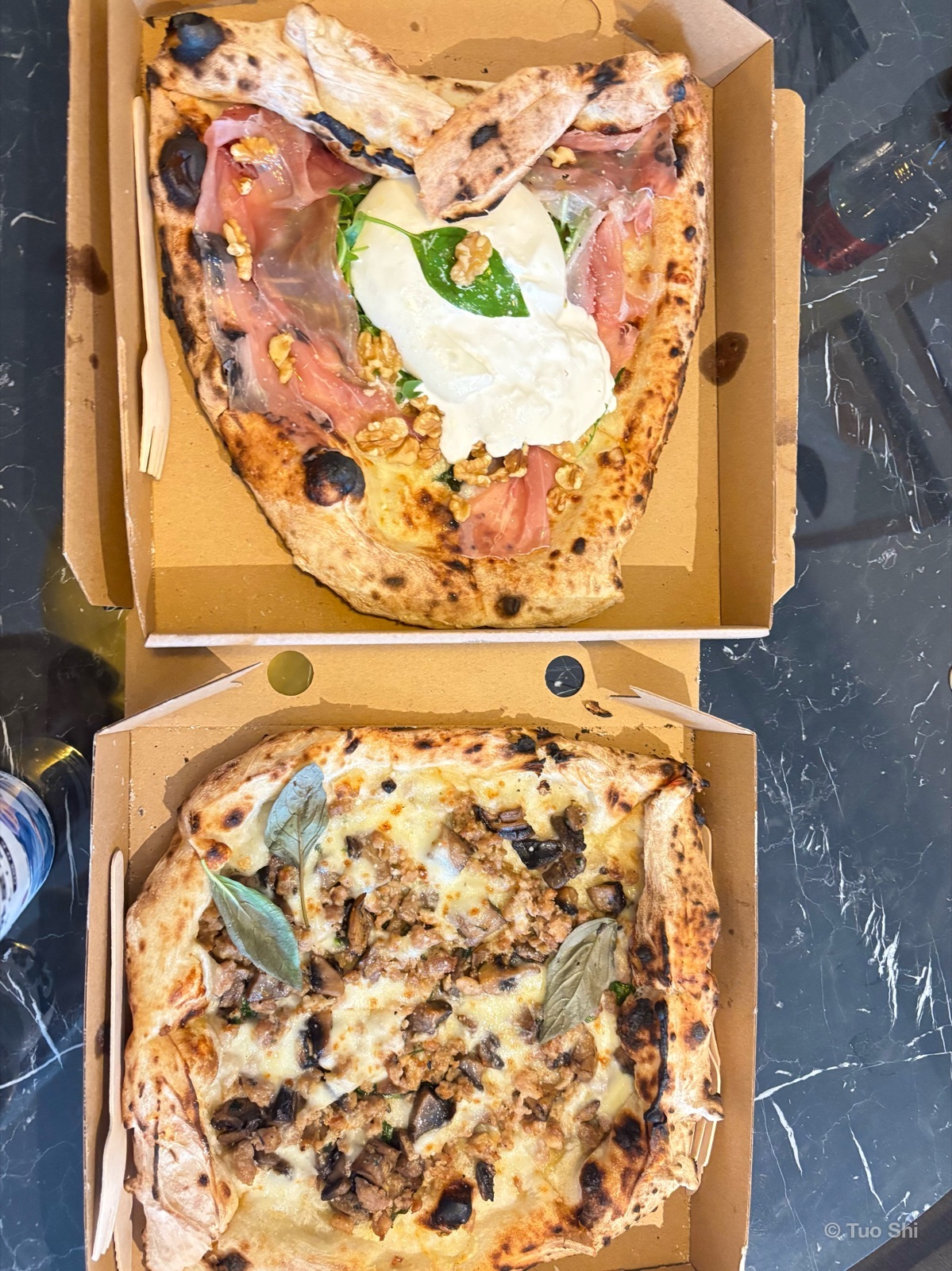 Two wood-fired pizzas in takeaway boxes, one with prosciutto and burrata, one with mushrooms and sage
