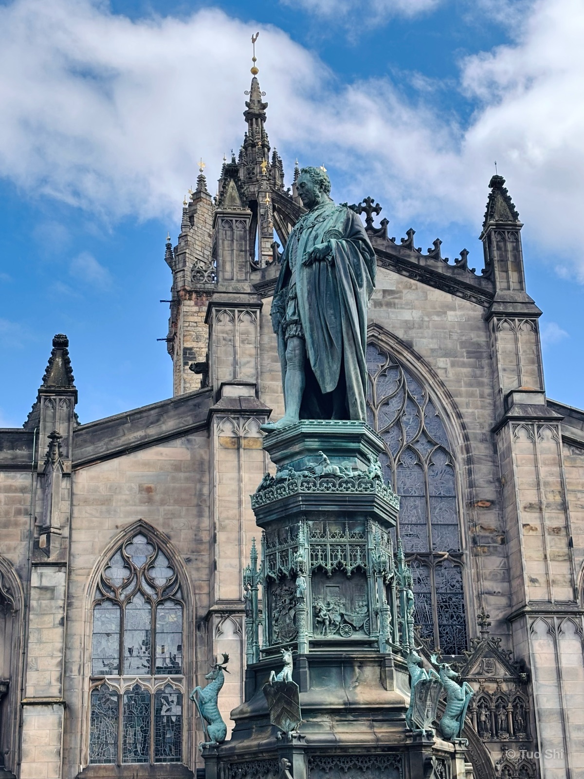 A bronze statue on a carved pedestal in front of the Gothic facade of St Giles' Cathedral