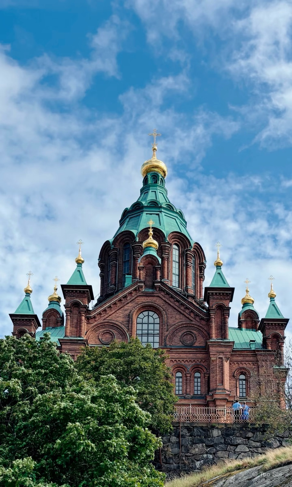 Uspenski Cathedral with its green and gold domes under a cloudy blue sky