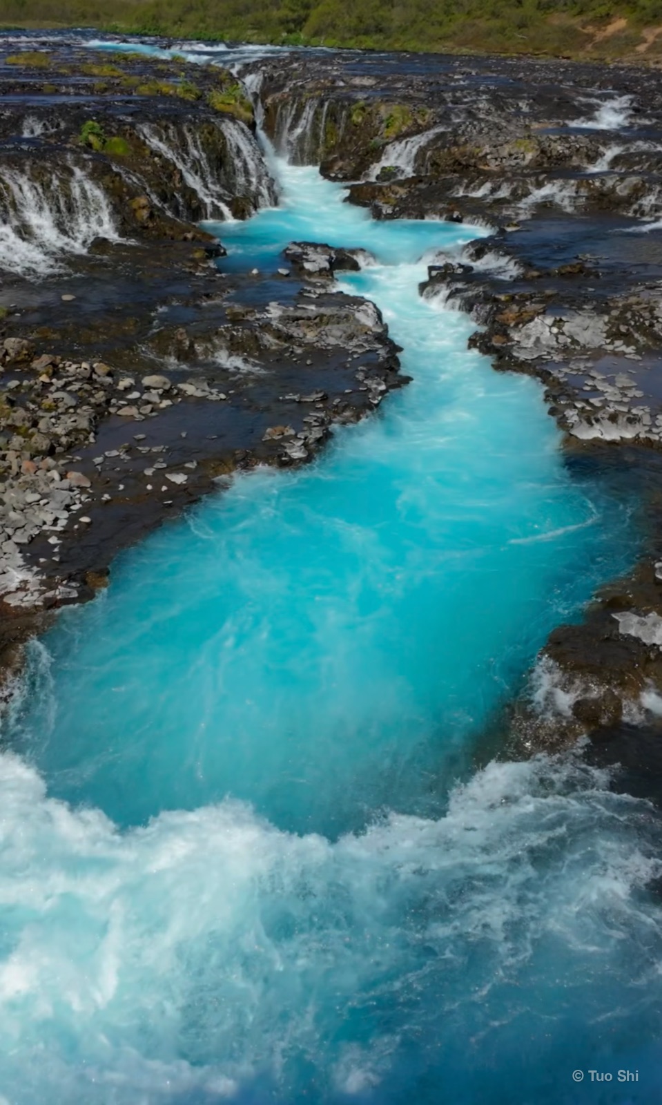 Bright turquoise water rushing through a rocky channel at Bruarfoss