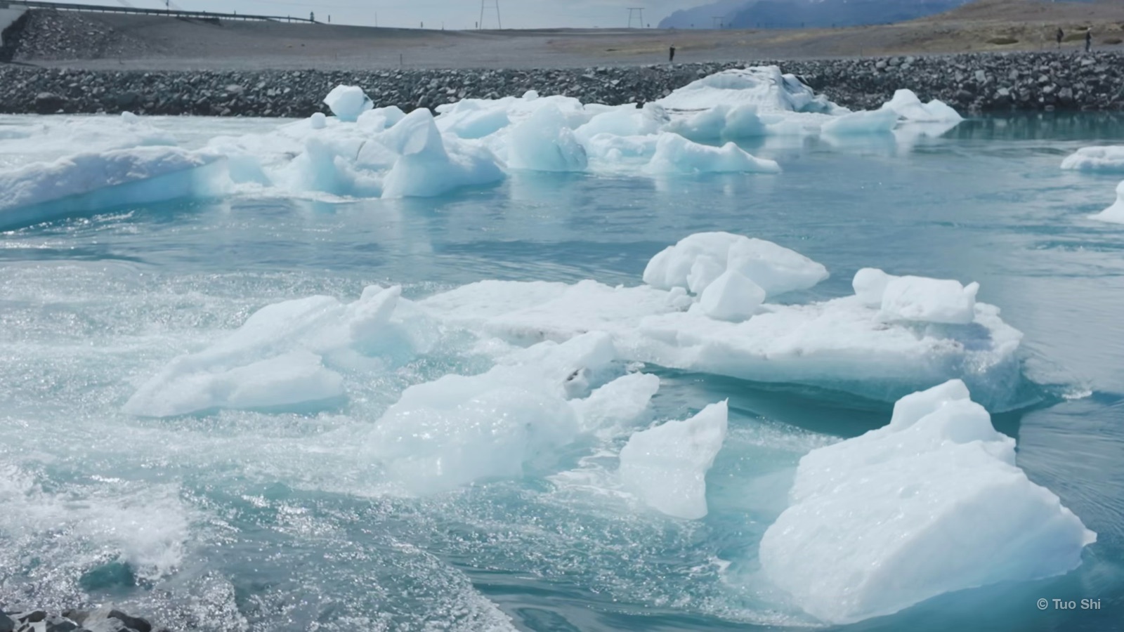 Blue-white icebergs floating in a glacier lagoon by a gravel shore