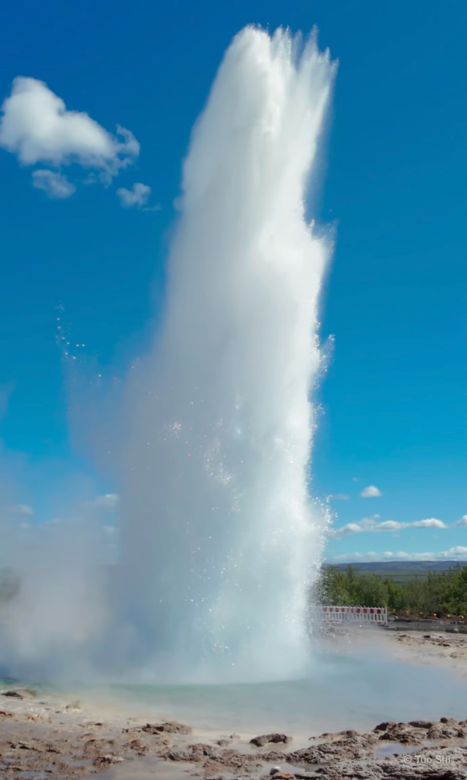 The Strokkur geyser erupting in a tall white column against a blue sky