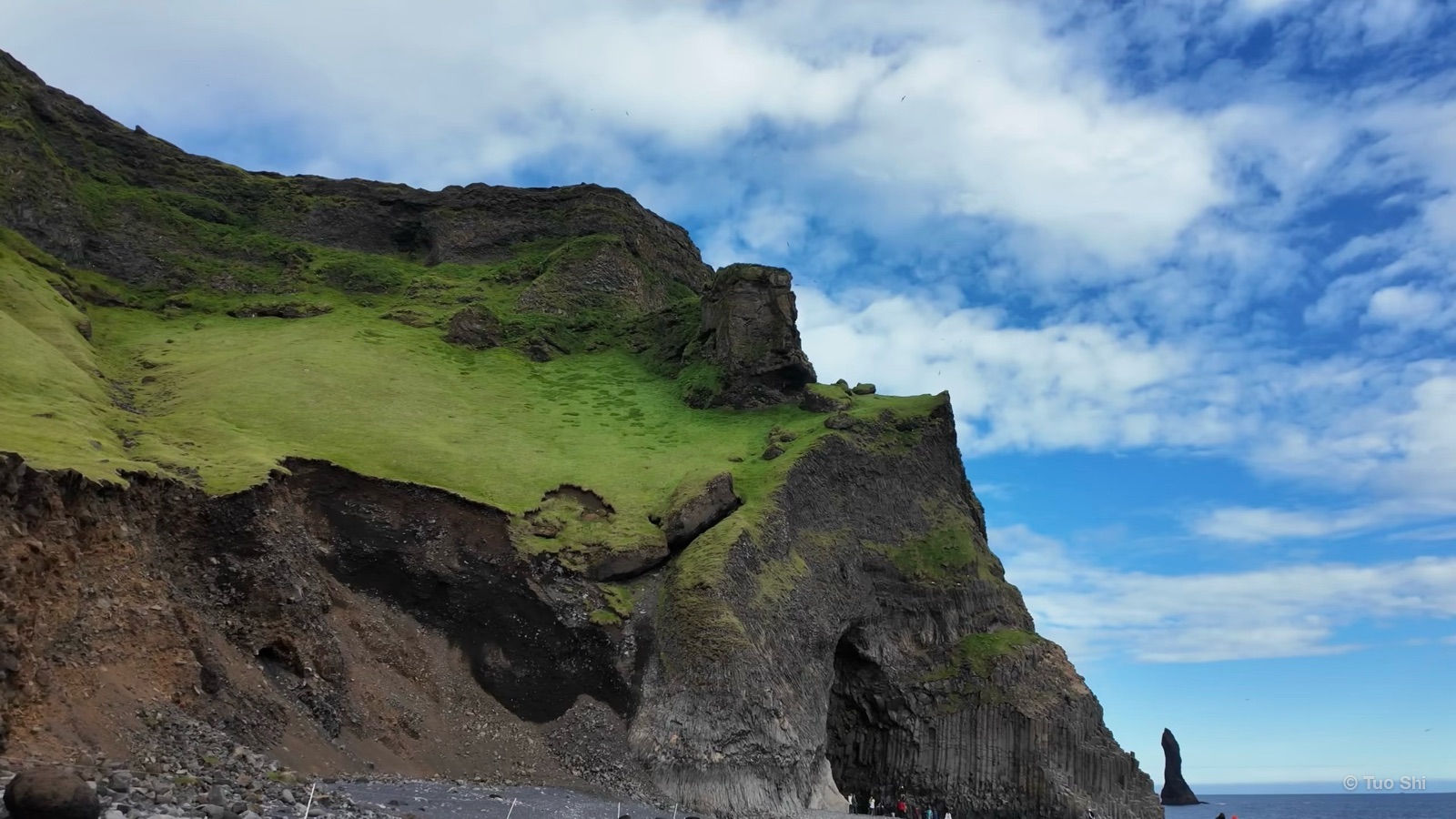 A grassy headland with dark cliffs and sea stacks on the coast