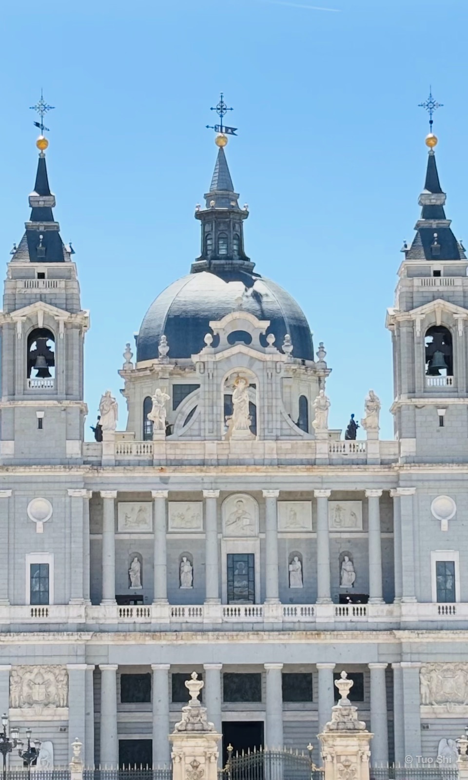 The white facade and grey dome of Almudena Cathedral against a clear blue sky