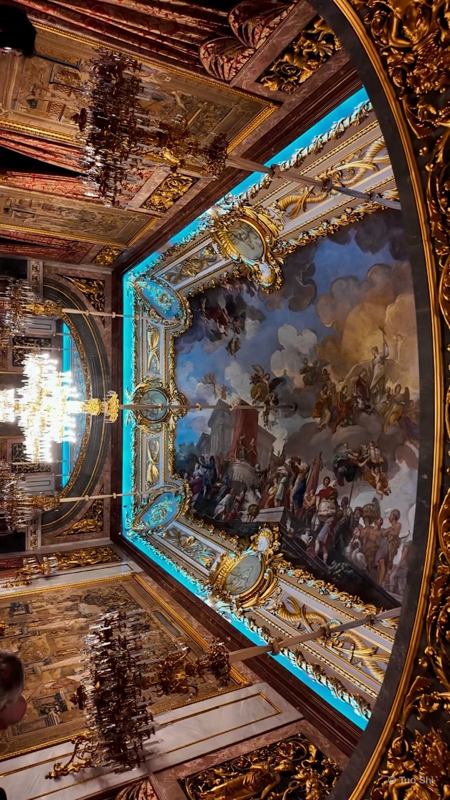 A gilded palace ceiling with a large fresco and crystal chandeliers