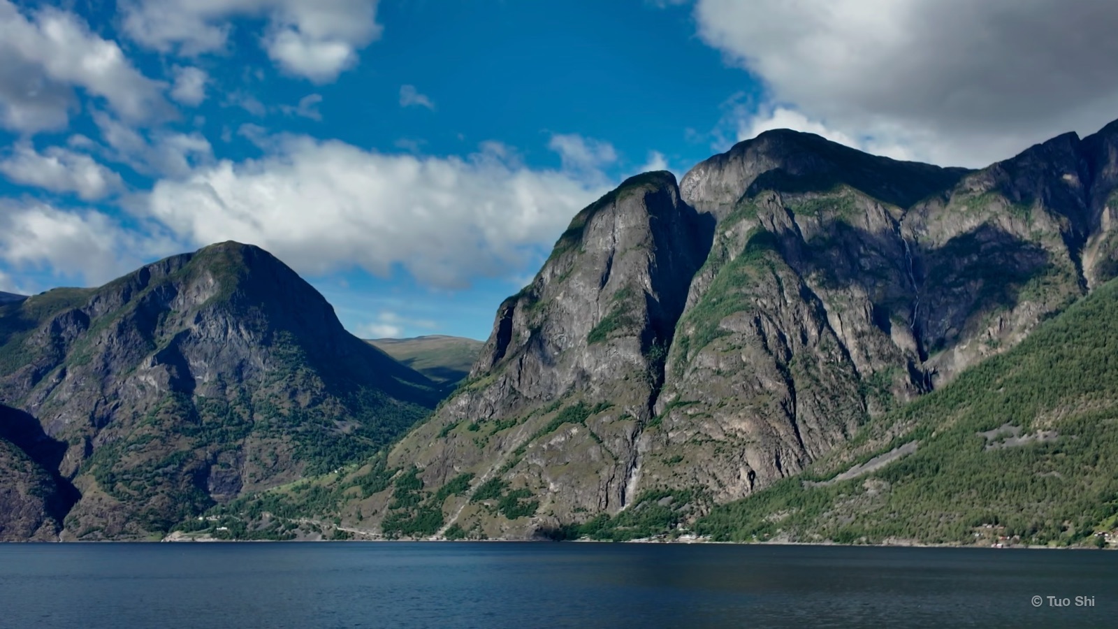 Jagged grey mountains rising from the water under white clouds