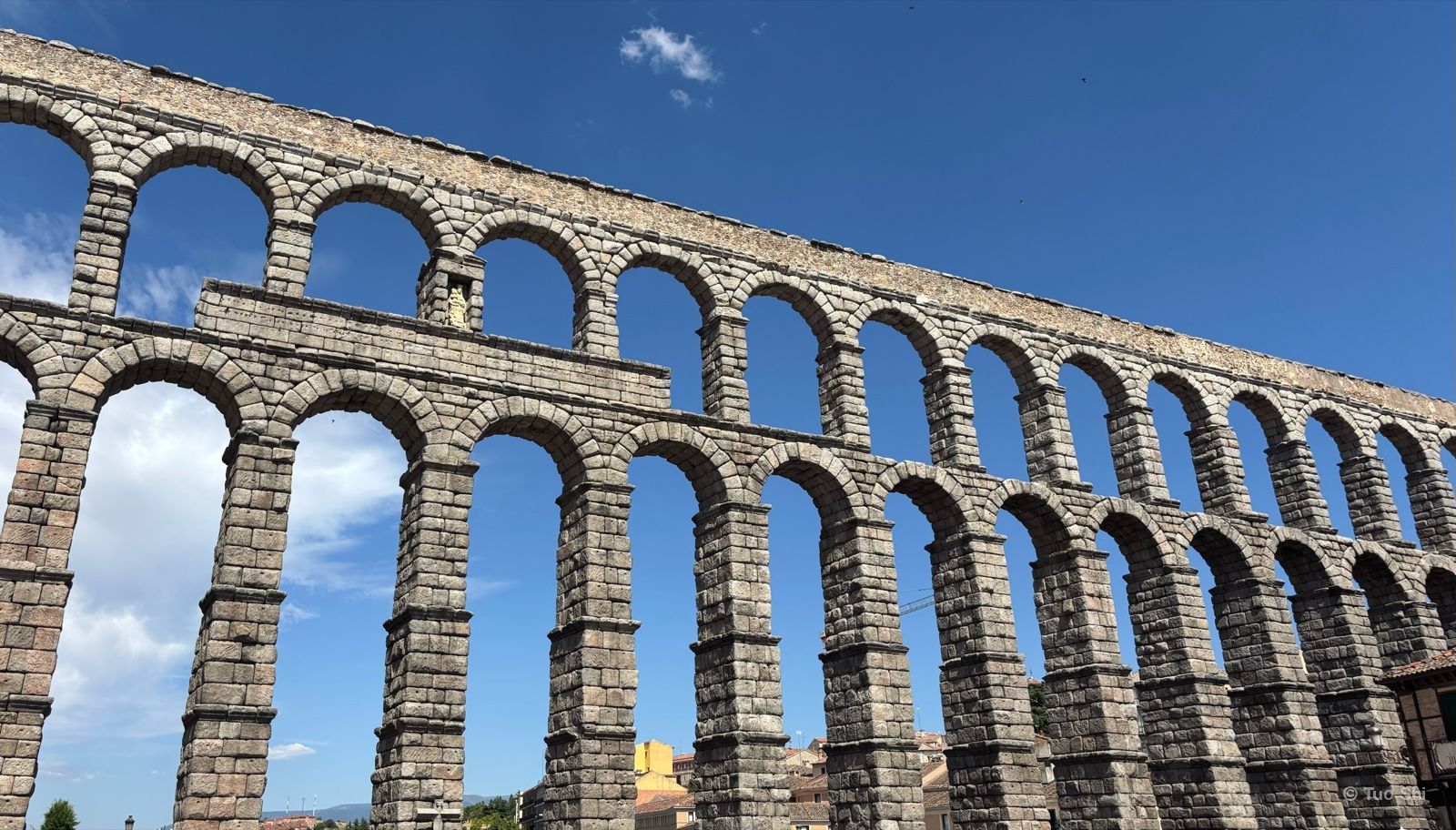 The tall granite arches of the Roman aqueduct of Segovia under a blue sky