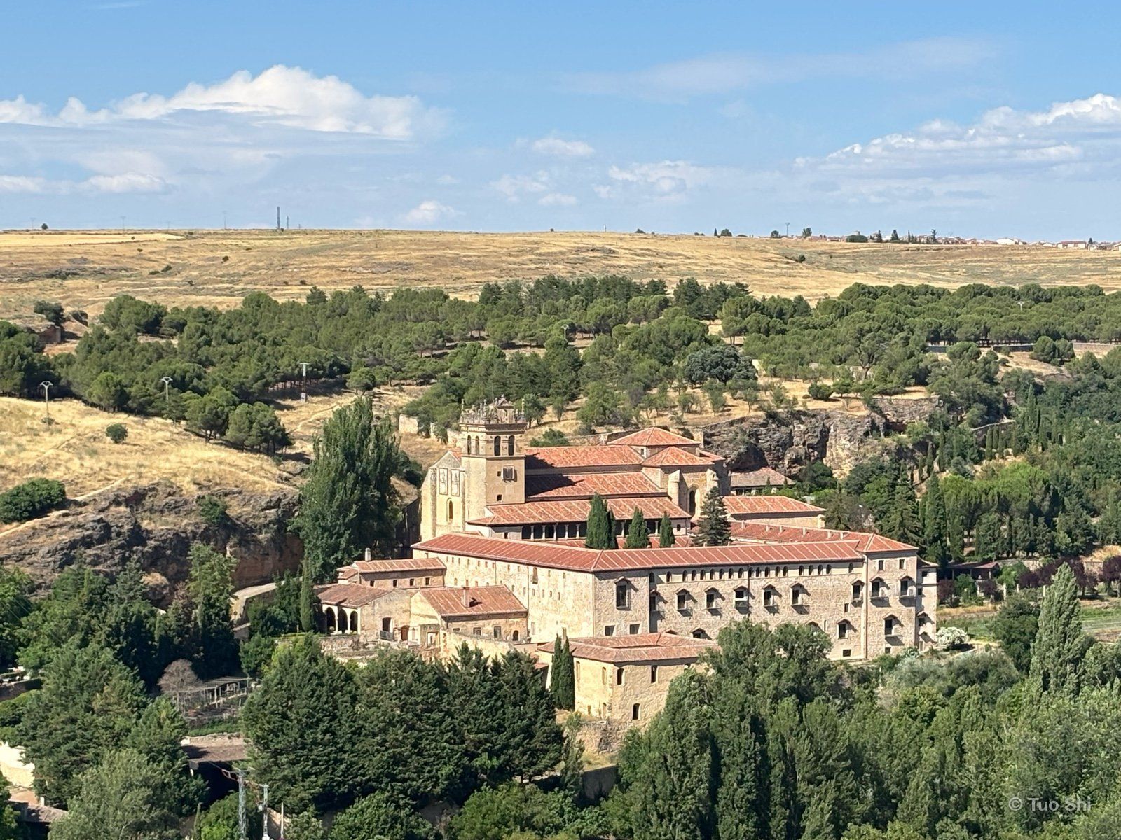 A monastery with red-tiled roofs in a green valley below dry golden hills